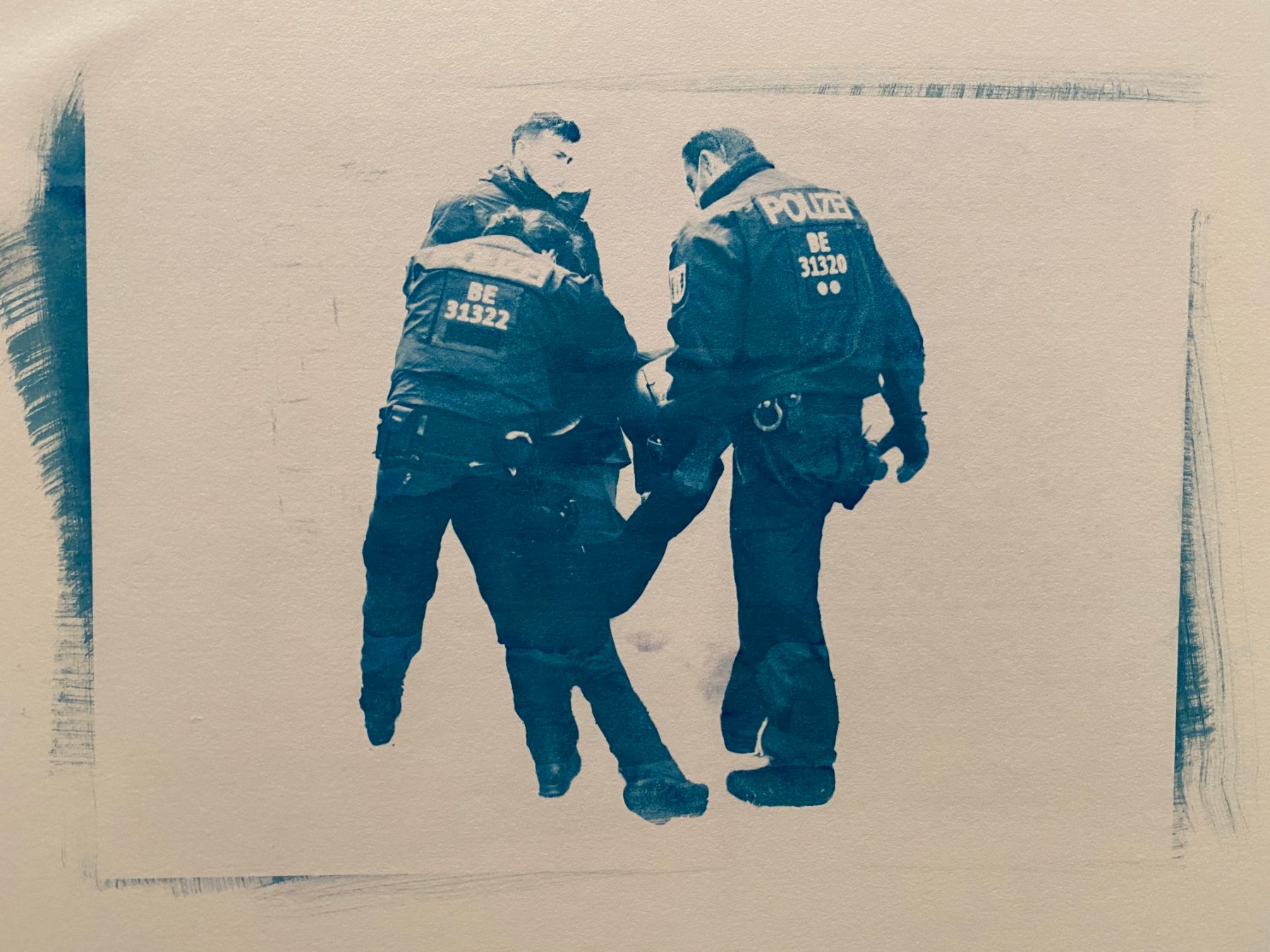 Cyanotypie: zwei Polizisten tragen eine Person fort.