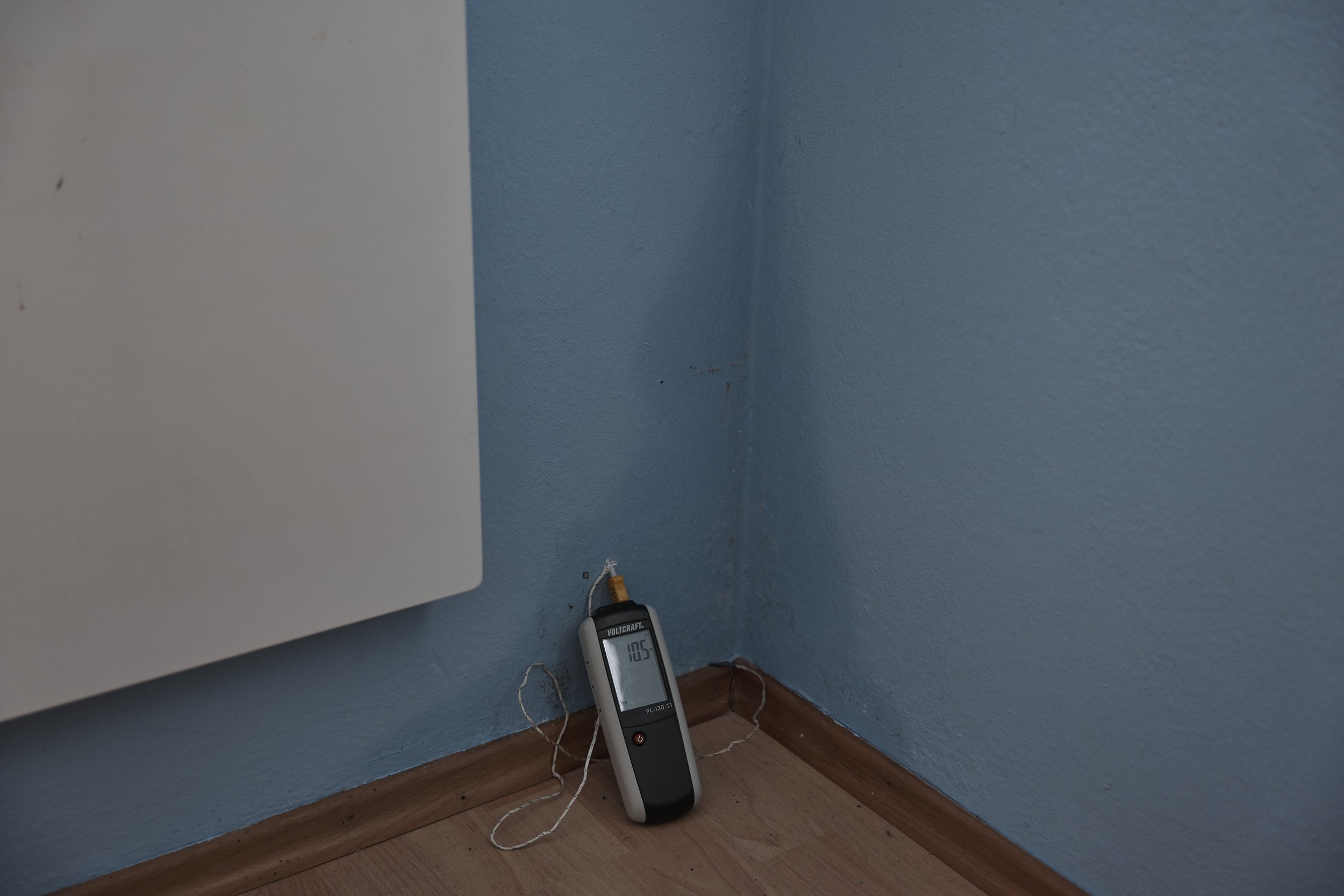 Ein Feuchtigkeits- und Temperaturmessgerät steht in der Ecke eines Zimmers an einer blauen Wand.