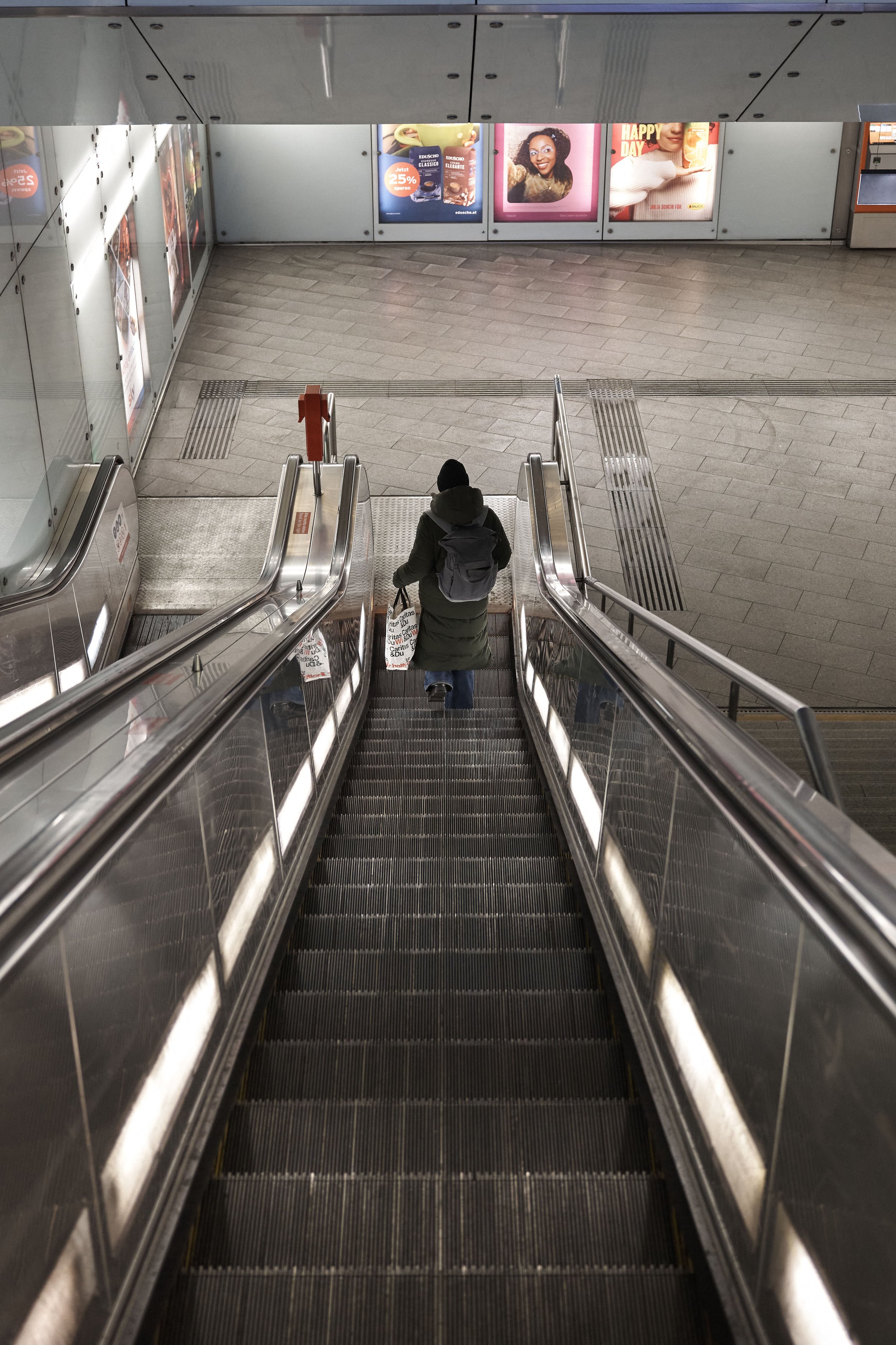 Eine Person im Wintermantel fährt auf einer Rolltreppe in einer U-Bahn-Station nach oben.